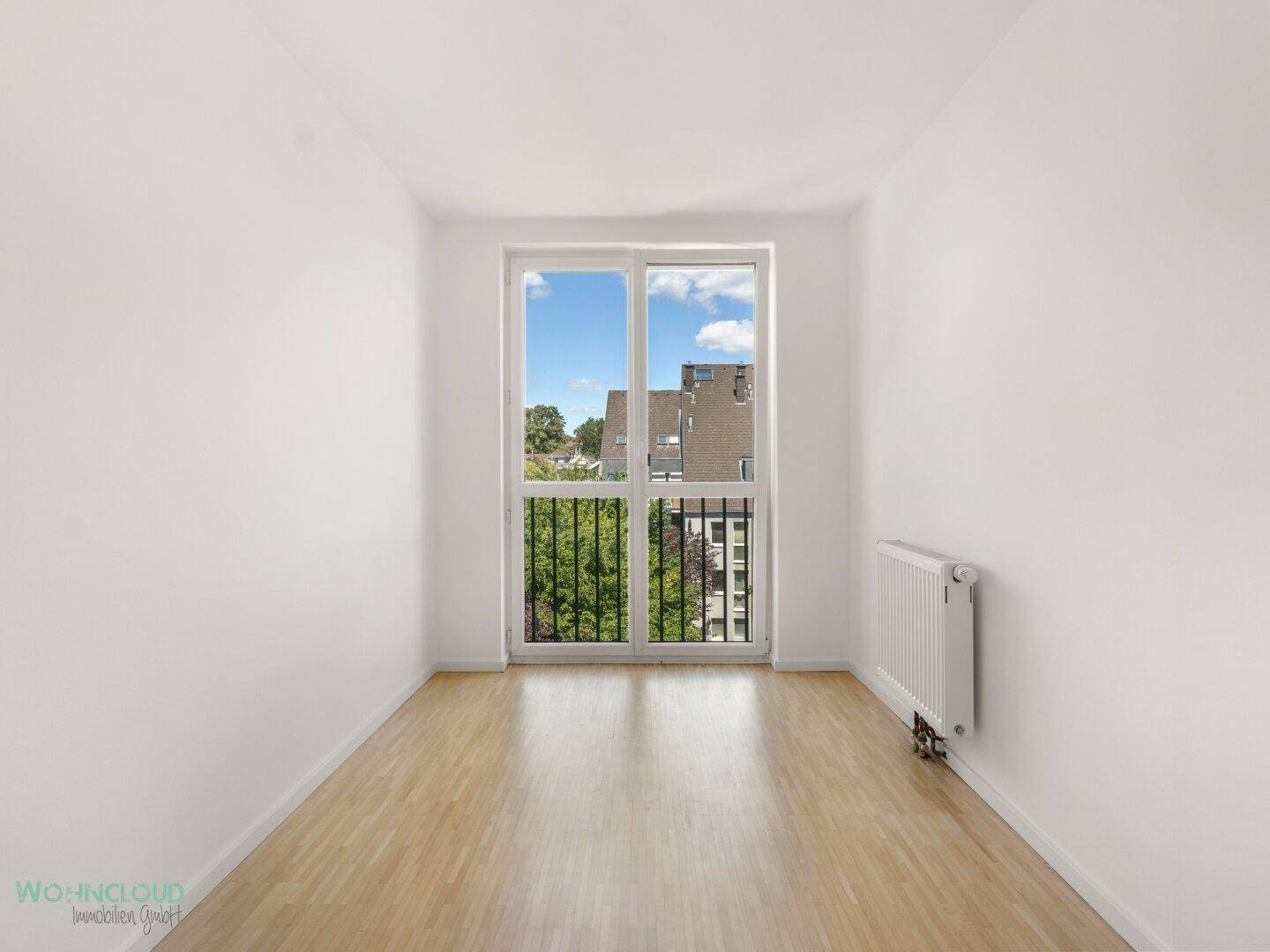 Leeres Schlafzimmer mit Parkettboden und französischem Balkon mit Grünblick.