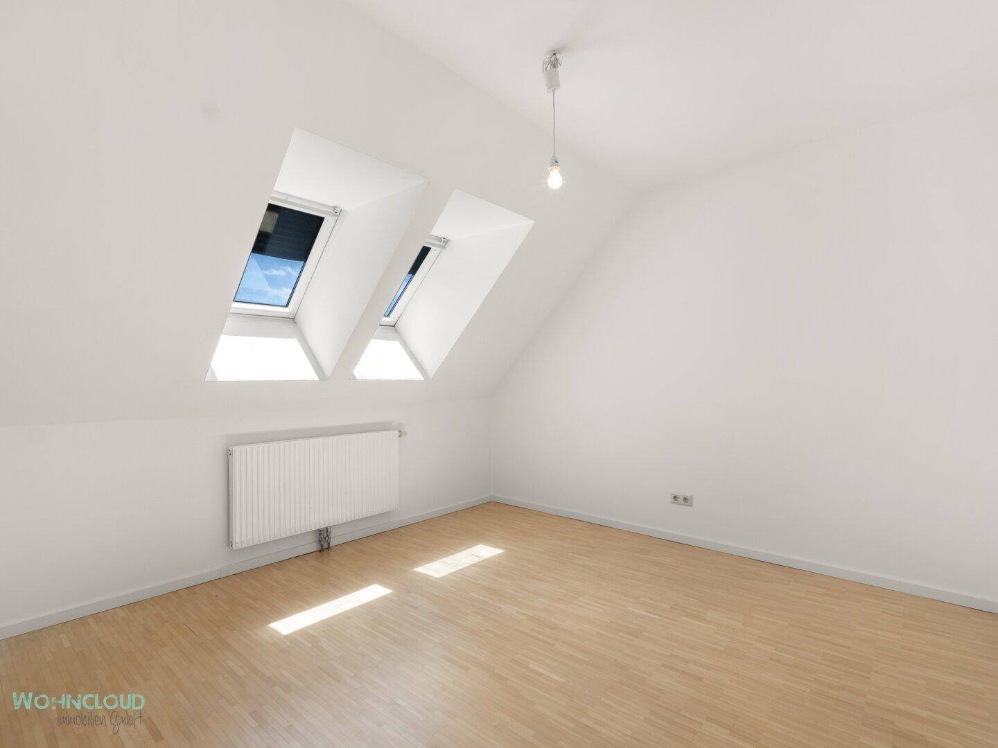Helles Dachgeschosszimmer mit zwei Dachfenstern, Schrägdach und Parkettboden.