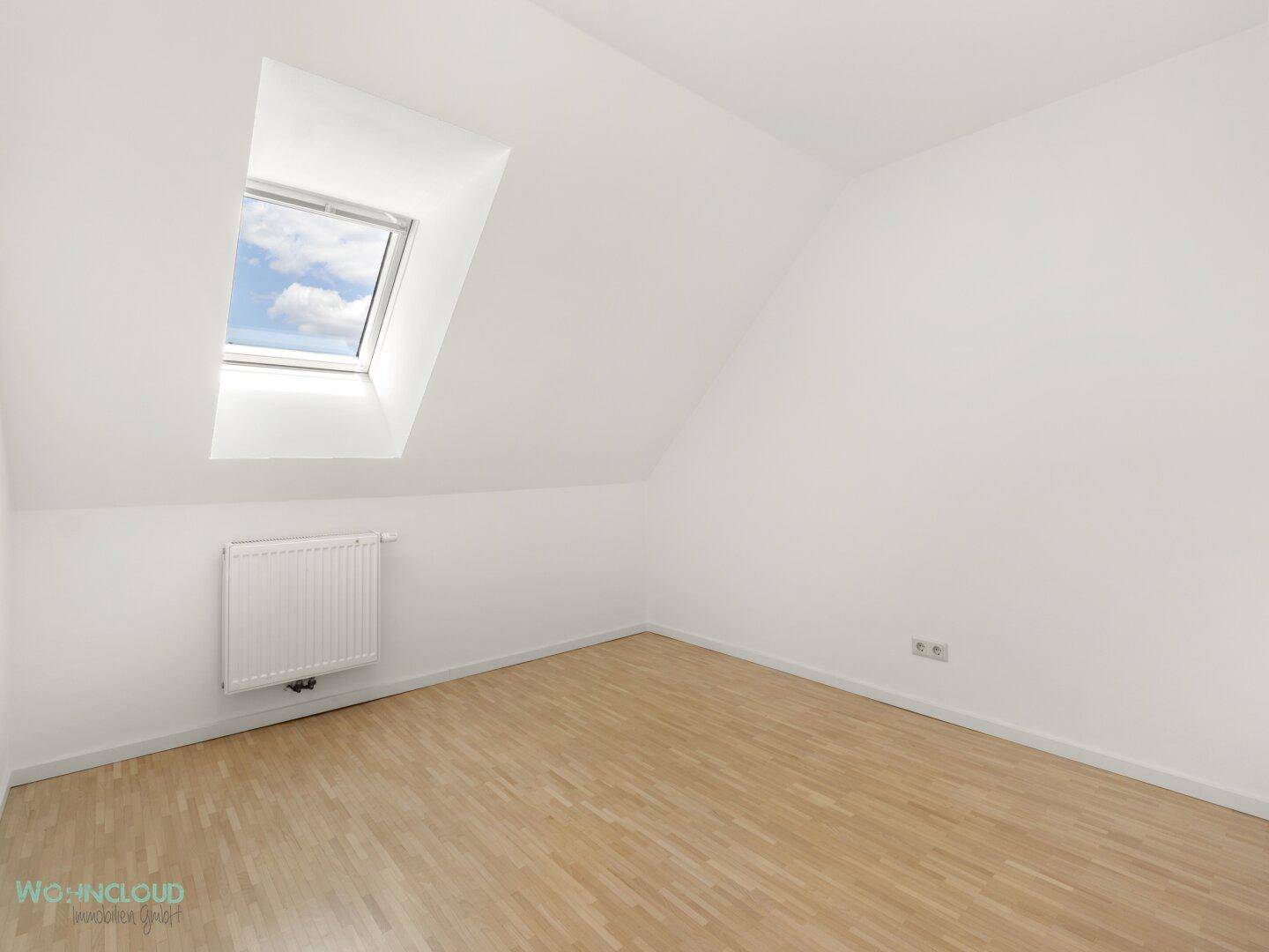 Helles Schlafzimmer im Dachgeschoss mit Schrägdach, Parkettboden und Dachfenster.