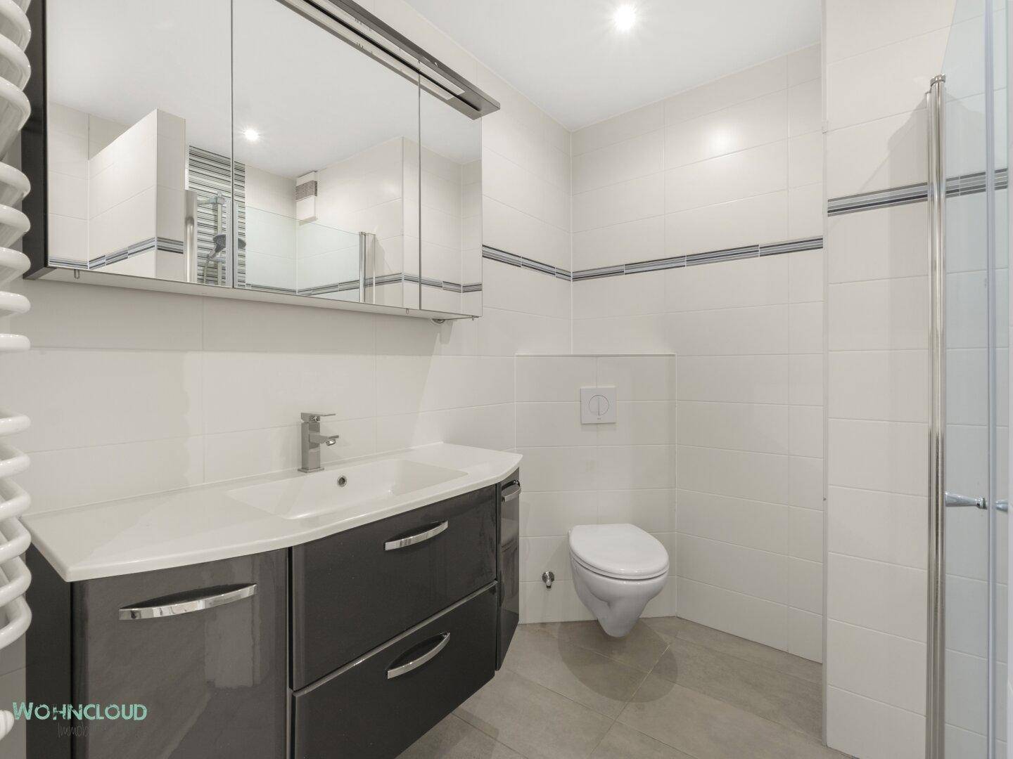 Modernes Badezimmer mit Waschtisch, Spiegelschrank, Dusche und weißen Fliesen.