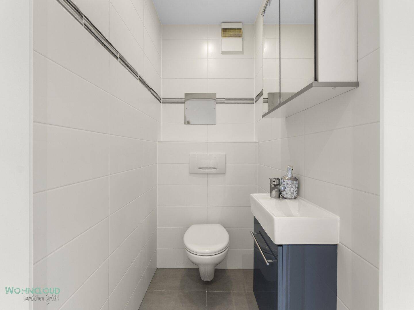 Kleines Gäste-WC mit Wand-WC, Waschbecken und weißen Fliesen.