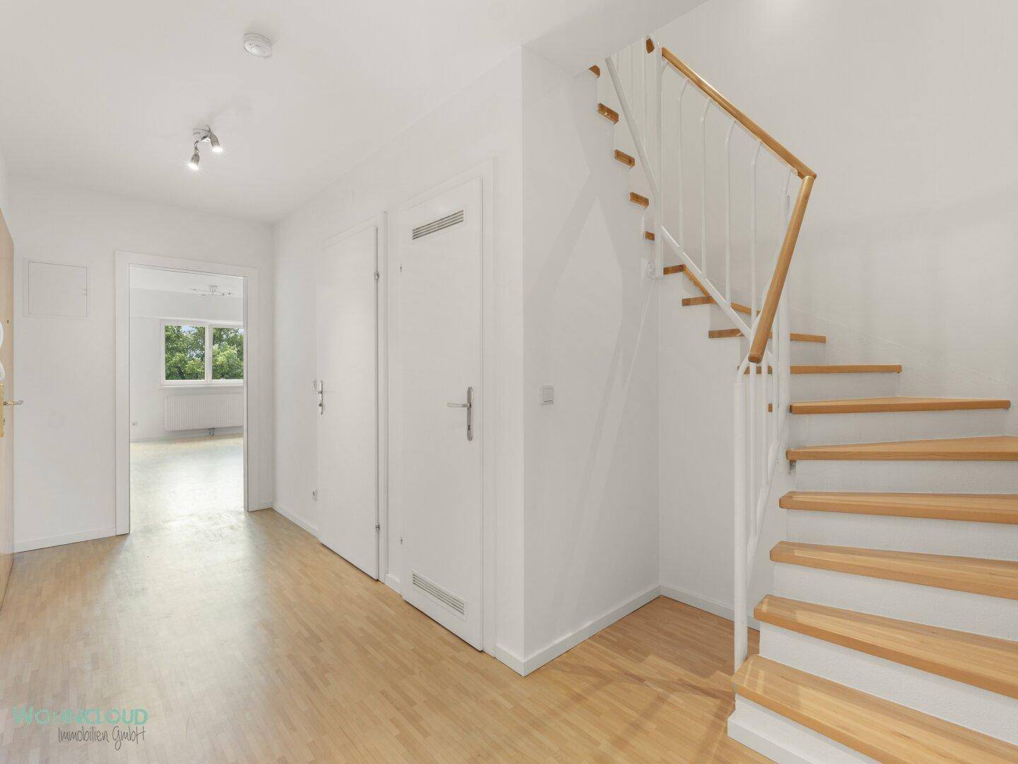 Heller Flur mit Holztreppe und Parkettboden, führt zu weiteren Räumen.