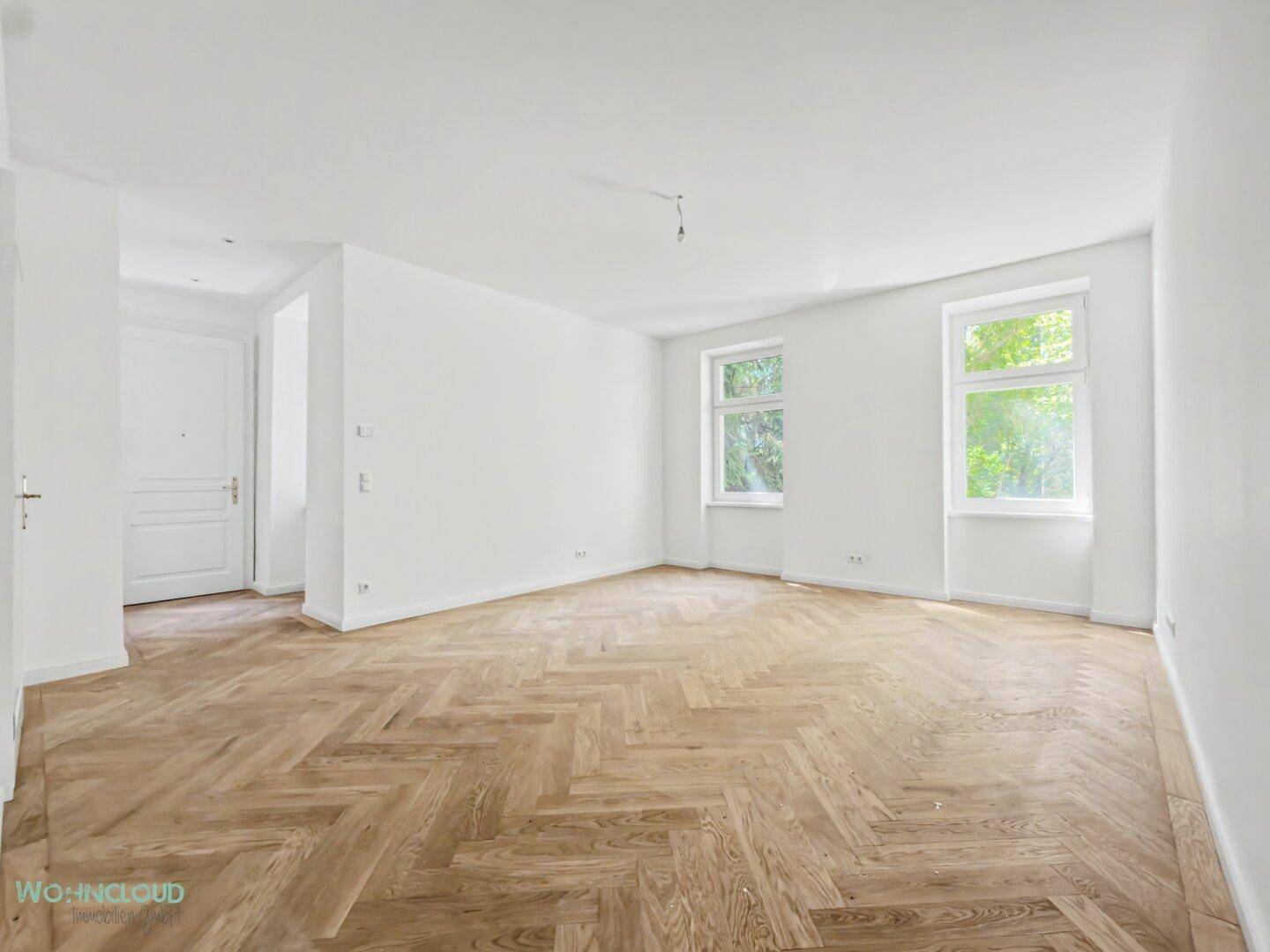 Geräumiges, leeres Zimmer mit Fischgrätparkett und hohen Decken, ideal für Wohnbereich.