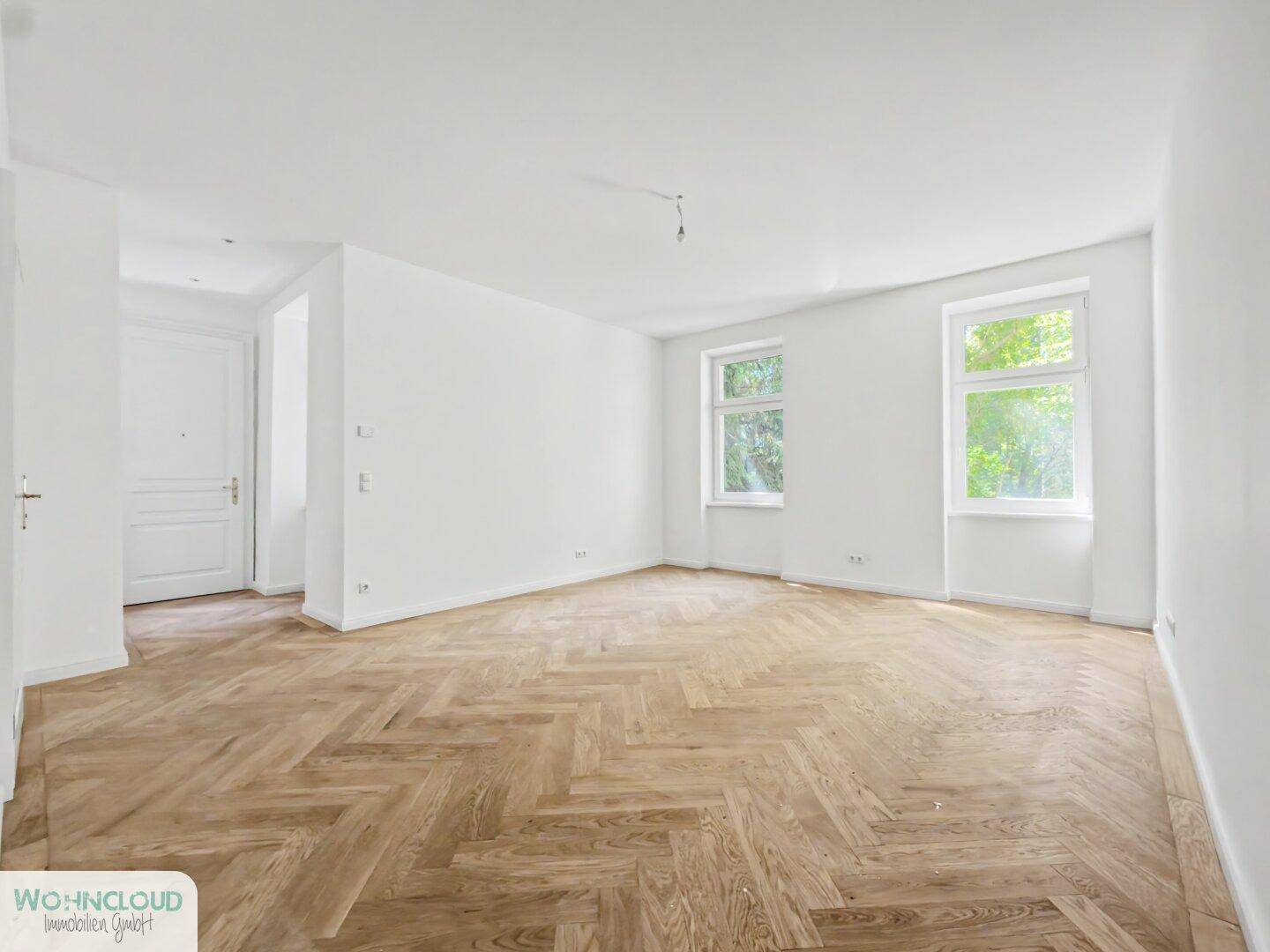Geräumiges, unmöbliertes Zimmer mit hellem Fischgrätparkett und hohen Fenstern, ideal für Wohnzwecke.