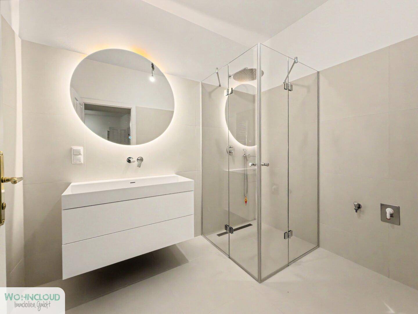Modernes Badezimmer mit schwebendem Waschtisch, beleuchtetem Spiegel und geräumiger Duschkabine.
