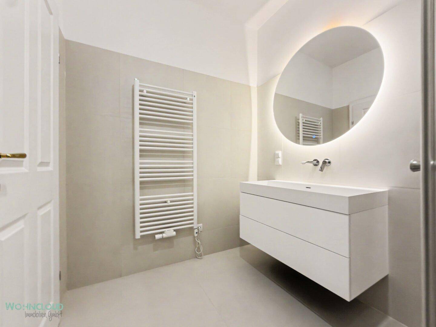Modernes Badezimmer mit schwebendem Waschtisch, beleuchtetem Spiegel und Handtuchheizkörper.