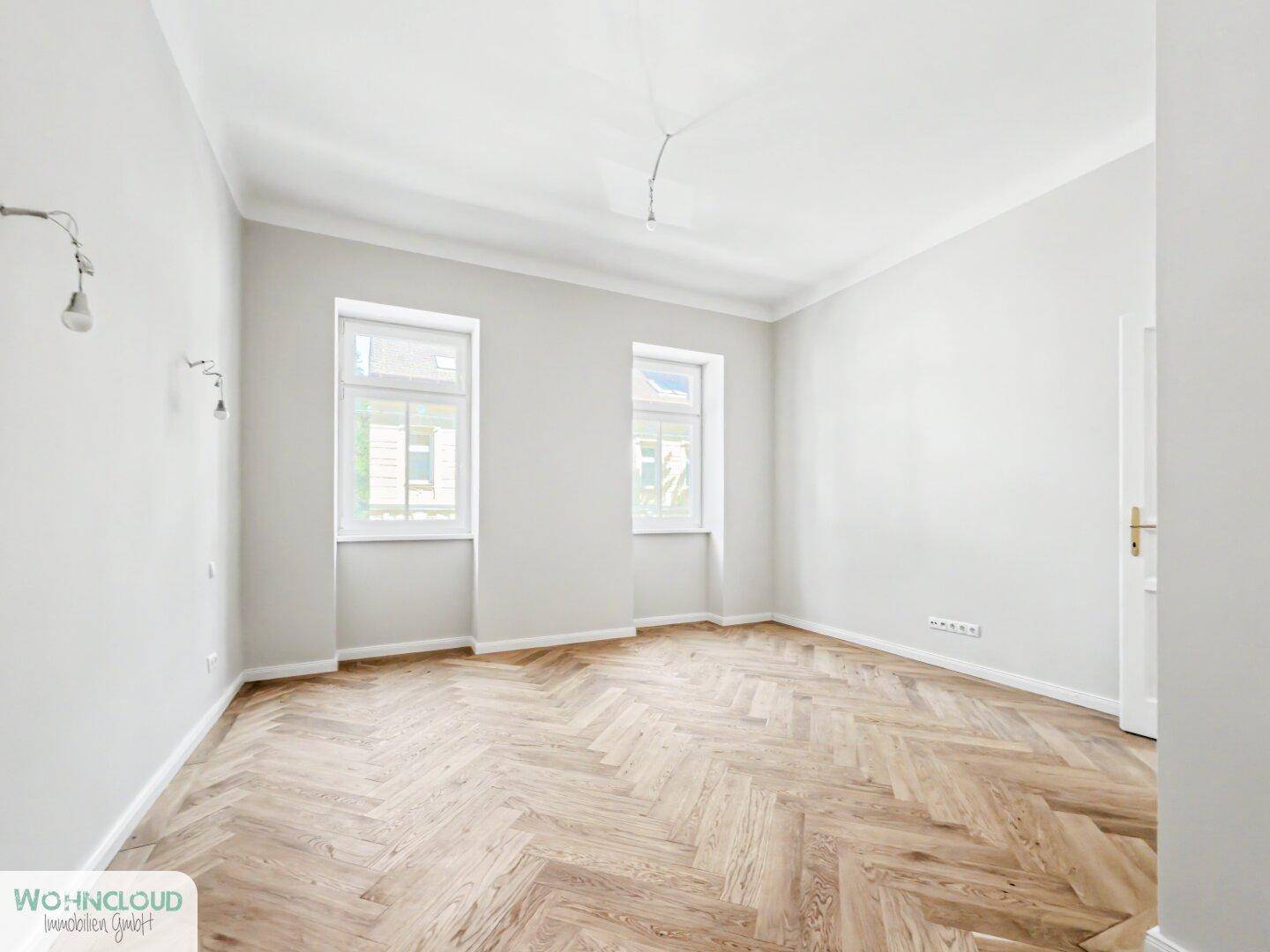 Leeres Schlafzimmer mit klassischem Fischgrätparkett und zwei Fenstern, bietet viel Gestaltungspotenzial.