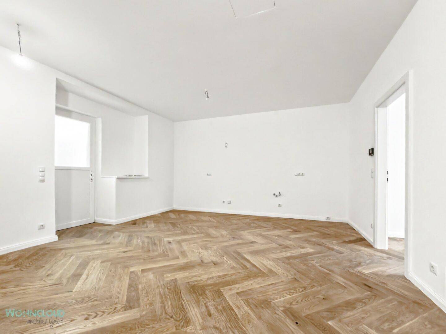 Geräumiges, leeres Zimmer mit Fischgrätparkett und weißen Wänden, vielseitig nutzbar.