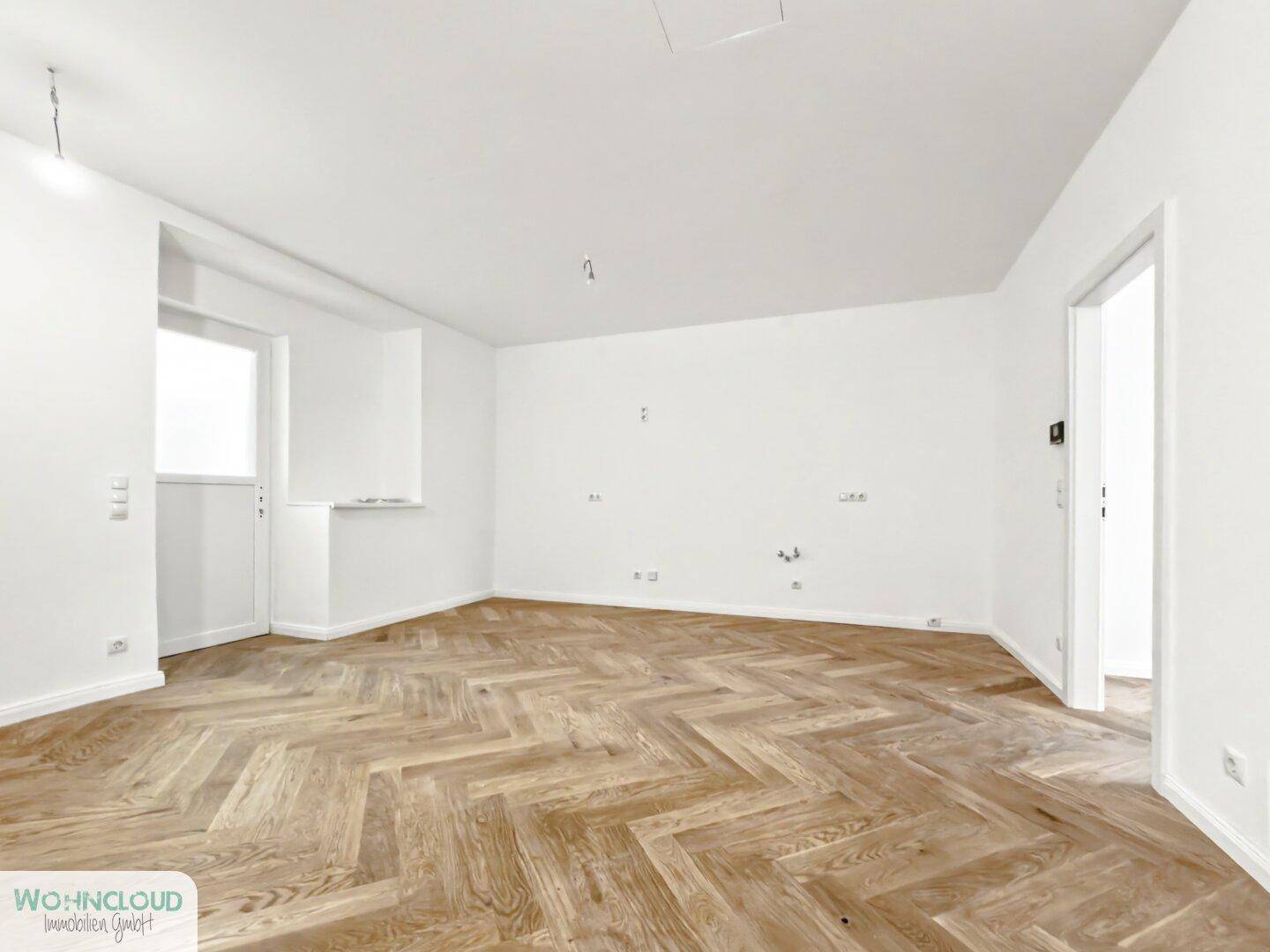 Geräumiges, unmöbliertes Zimmer mit Fischgrätparkett und weiß gestrichenen Wänden, vielseitig nutzbar.