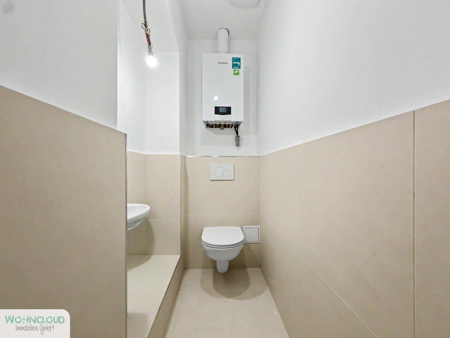 Funktionale Gästetoilette mit wandhängendem WC, kleinem Waschbecken und Warmwasserbereiter.