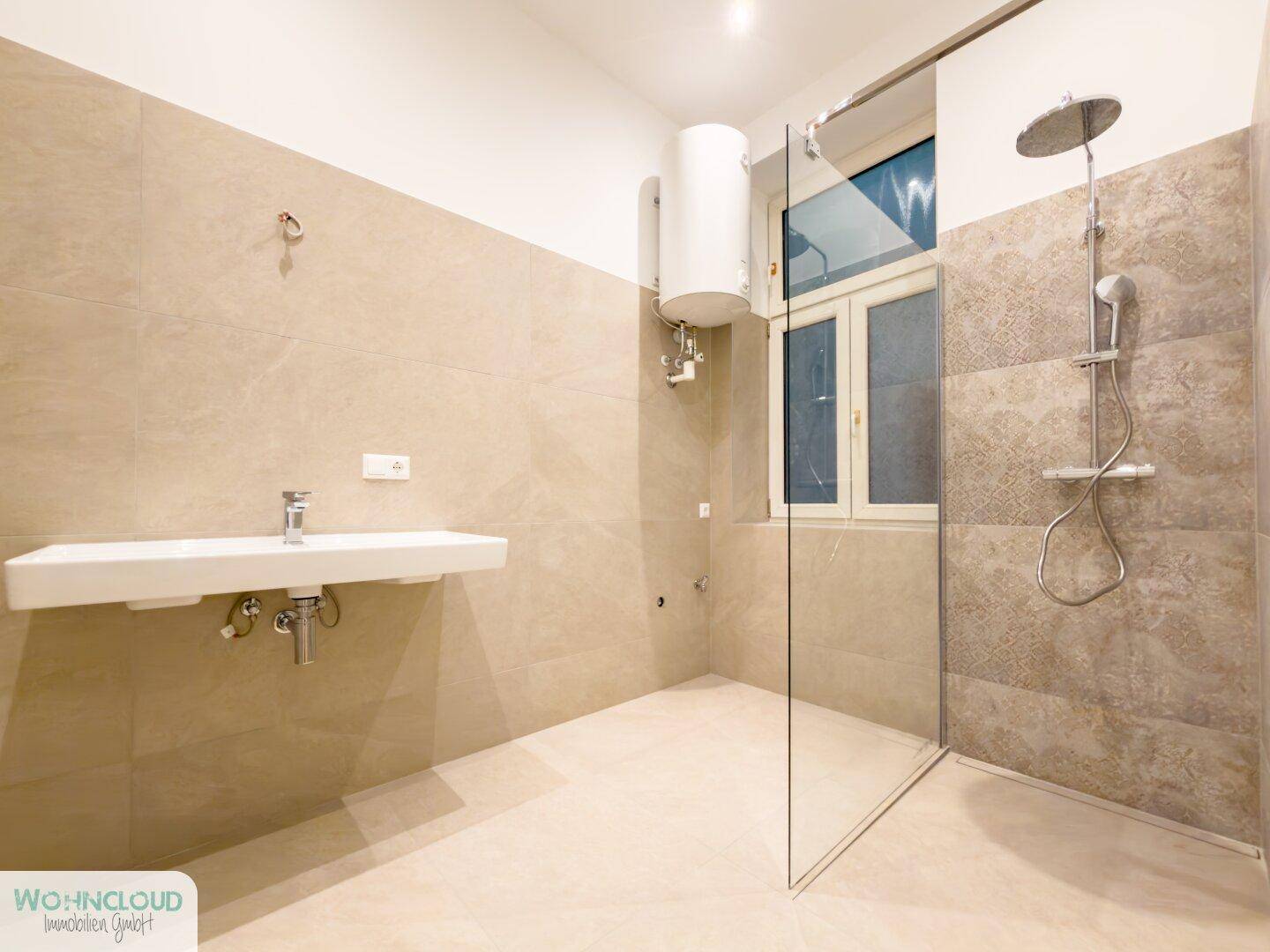 Geräumiges Badezimmer mit moderner begehbarer Dusche und vorbereitetem Bereich für ein Waschbecken.