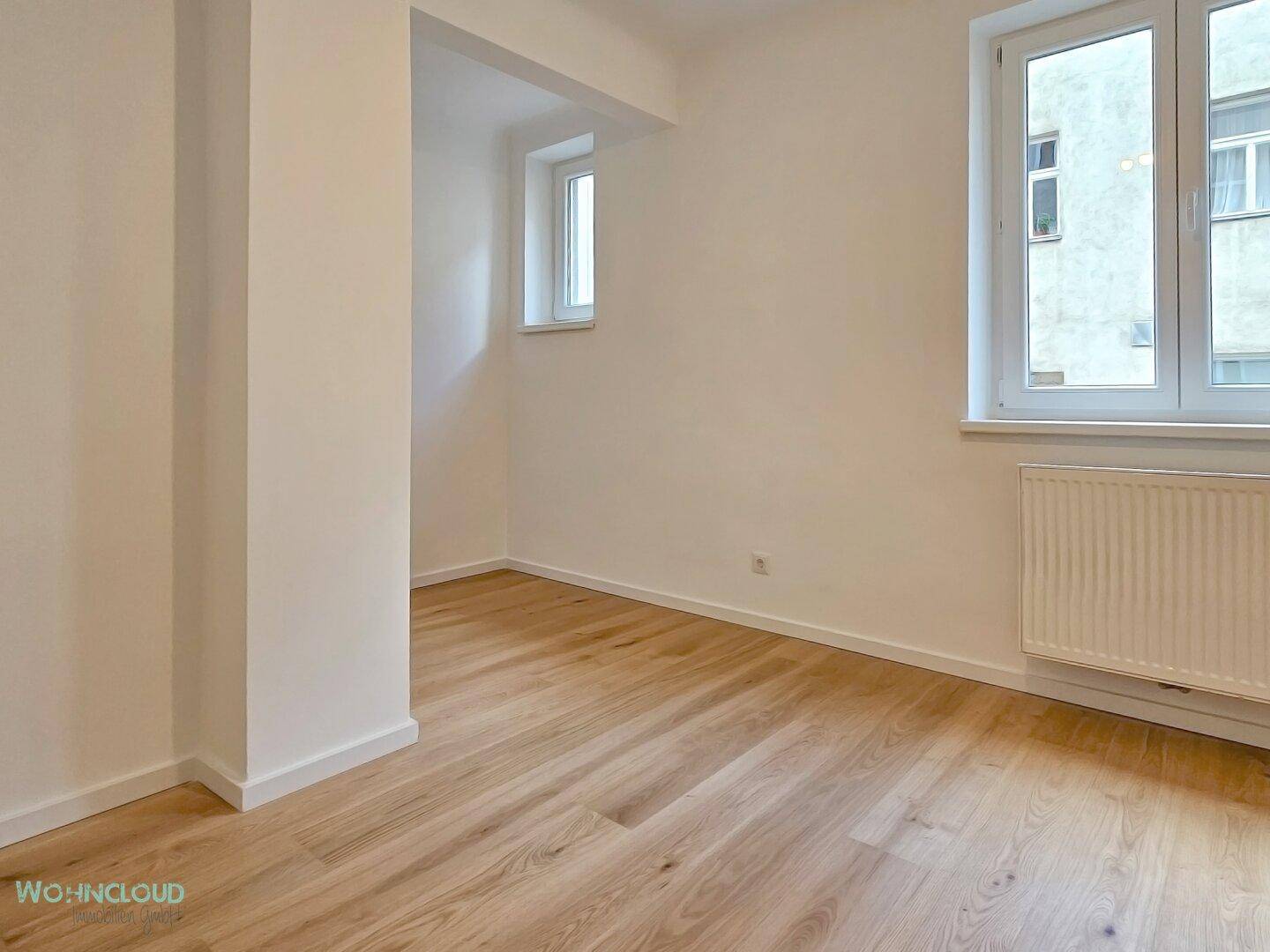 Leerer Raum mit hellem Holzparkettboden, weißen Wänden und zwei Fenstern, ideal als Schlaf- oder Arbeitszimmer.