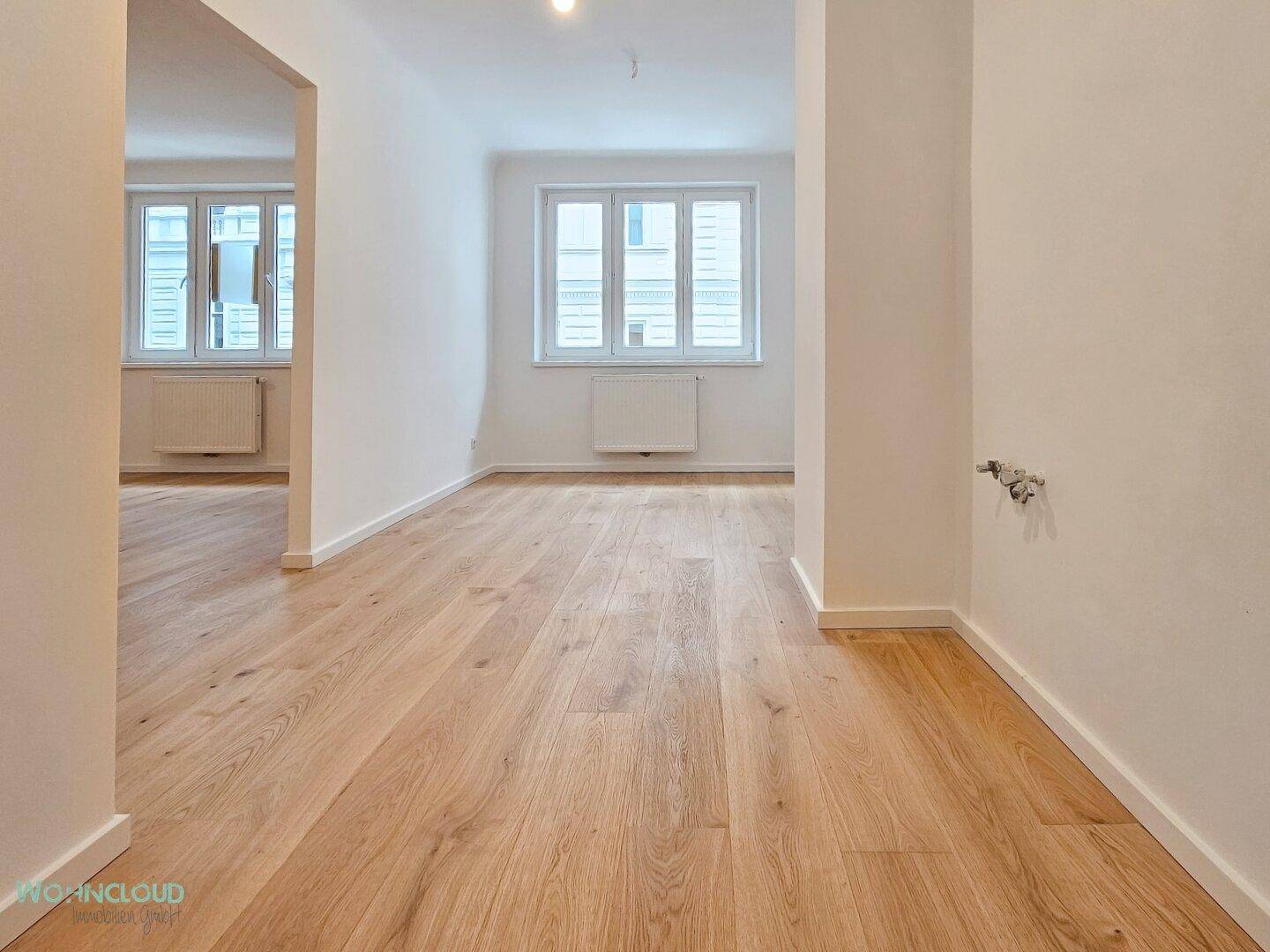 Heller Flur mit neuem Holzparkettboden und Blick in einen weiteren Raum mit Fenstern.