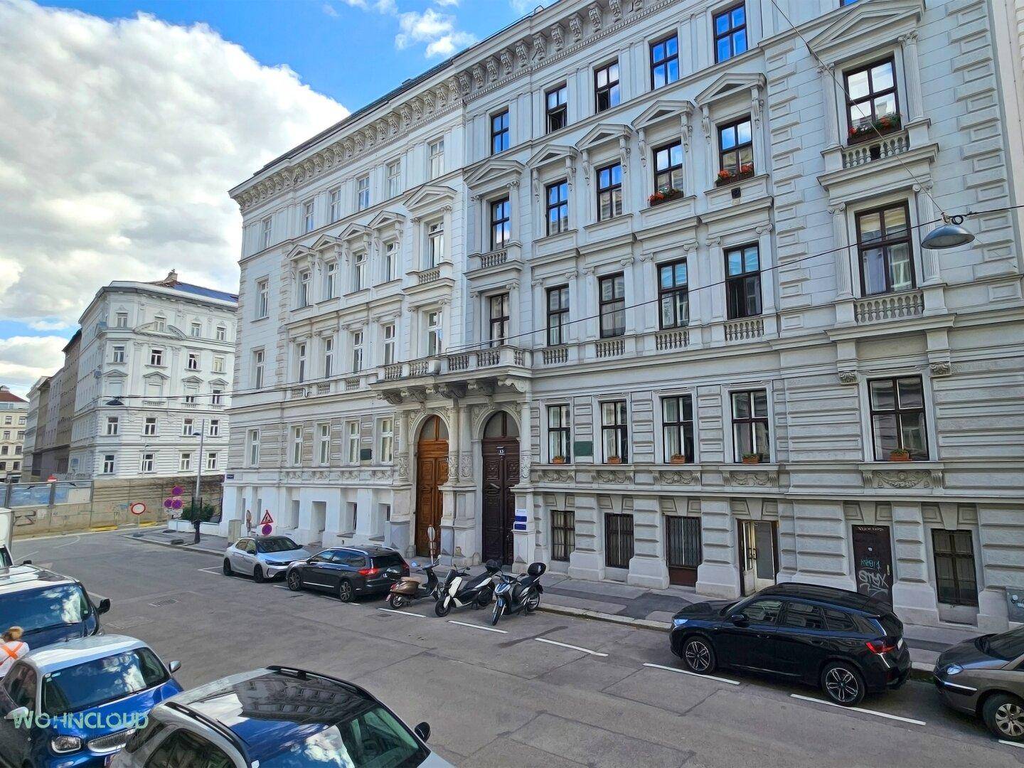 Historische, reich verzierte Fassade eines Altbaus an einer städtischen Straße mit parkenden Autos.