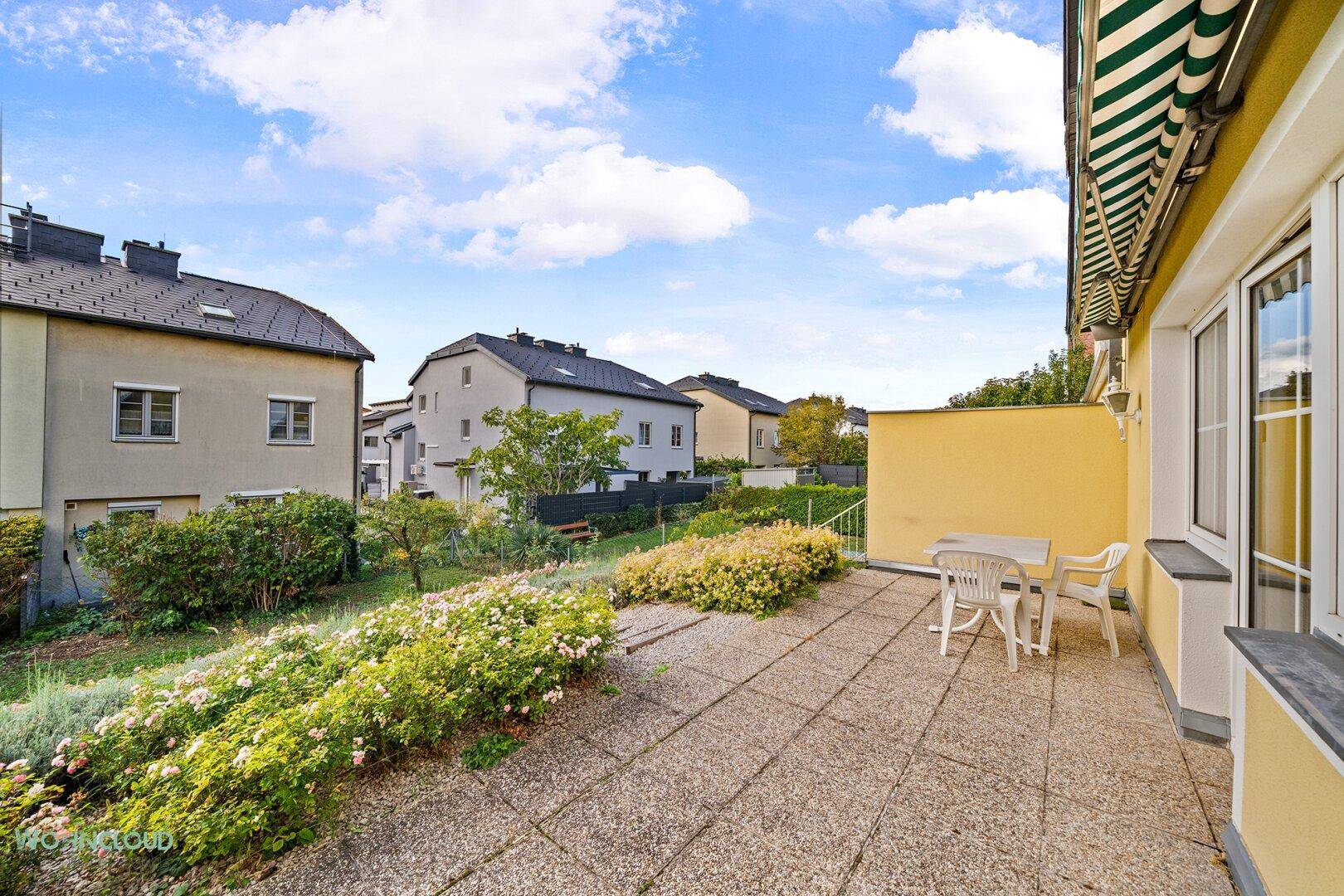 Große gepflasterte Terrasse mit Markise und Blick auf die umliegende Nachbarschaft.