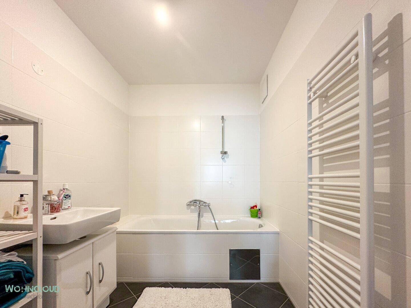 Helles Badezimmer mit Badewanne, Waschbecken und praktischem Handtuchheizkörper.