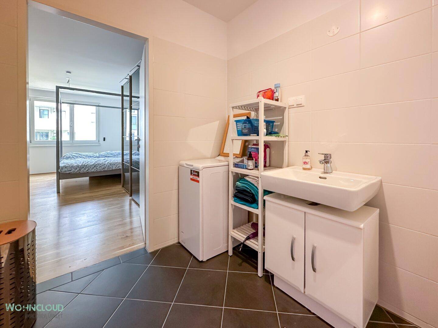Modernes Badezimmer mit Waschbecken, Waschmaschine und Zugang zu einem Schlafzimmer.