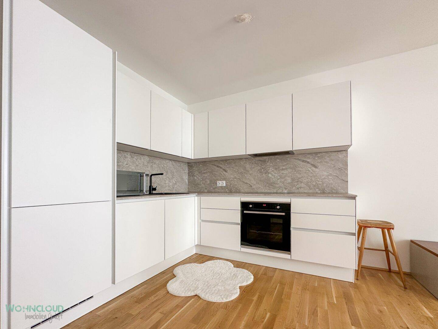 Moderne Einbauküche mit weißen Hochglanzfronten, grauer Arbeitsplatte und integriertem Backofen.