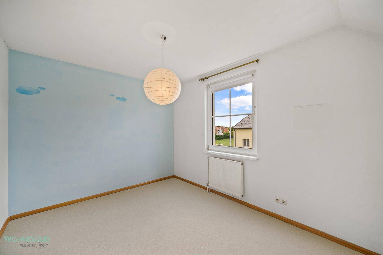 Kinderzimmer mit Teppichboden, blauer Wandgestaltung und einem Fenster für Tageslicht.