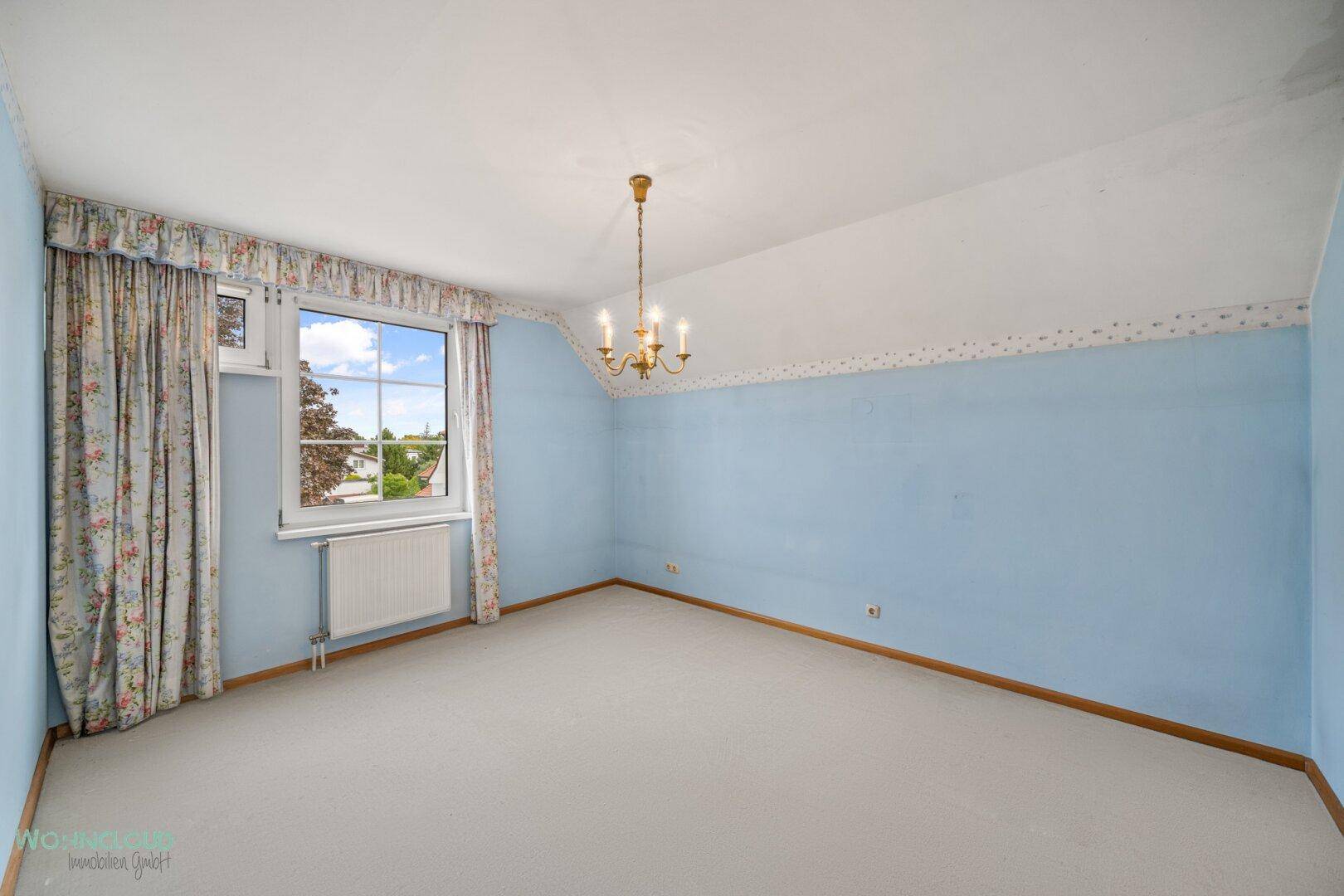 Schlafzimmer mit Teppichboden, blauen Wänden und einem Fenster mit Blick ins Grüne.