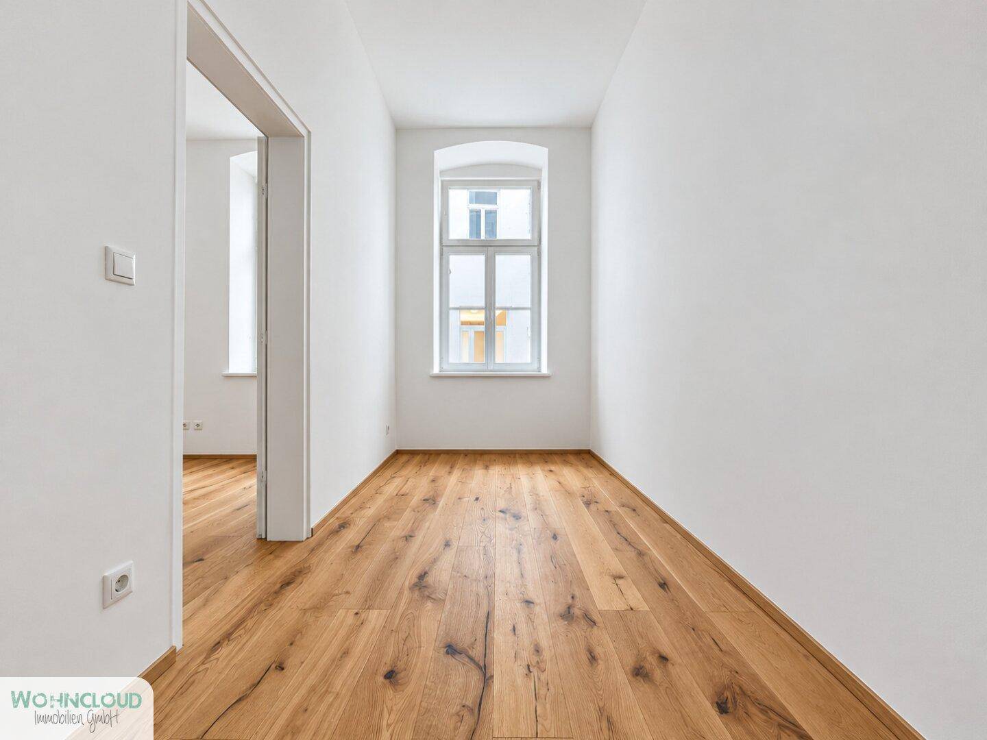 Langer, heller Flur mit Holzboden und einem Fenster, das Tageslicht hereinlässt.