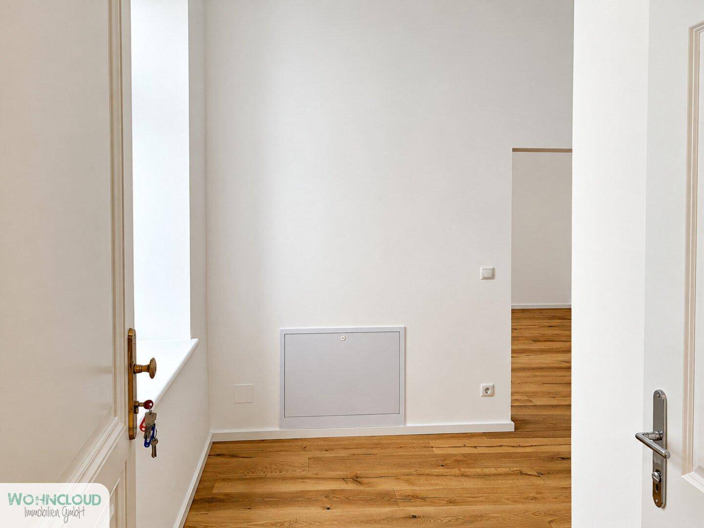 Heller Bereich mit Holzboden und einer Wandöffnung, die zu weiteren Räumen führt.