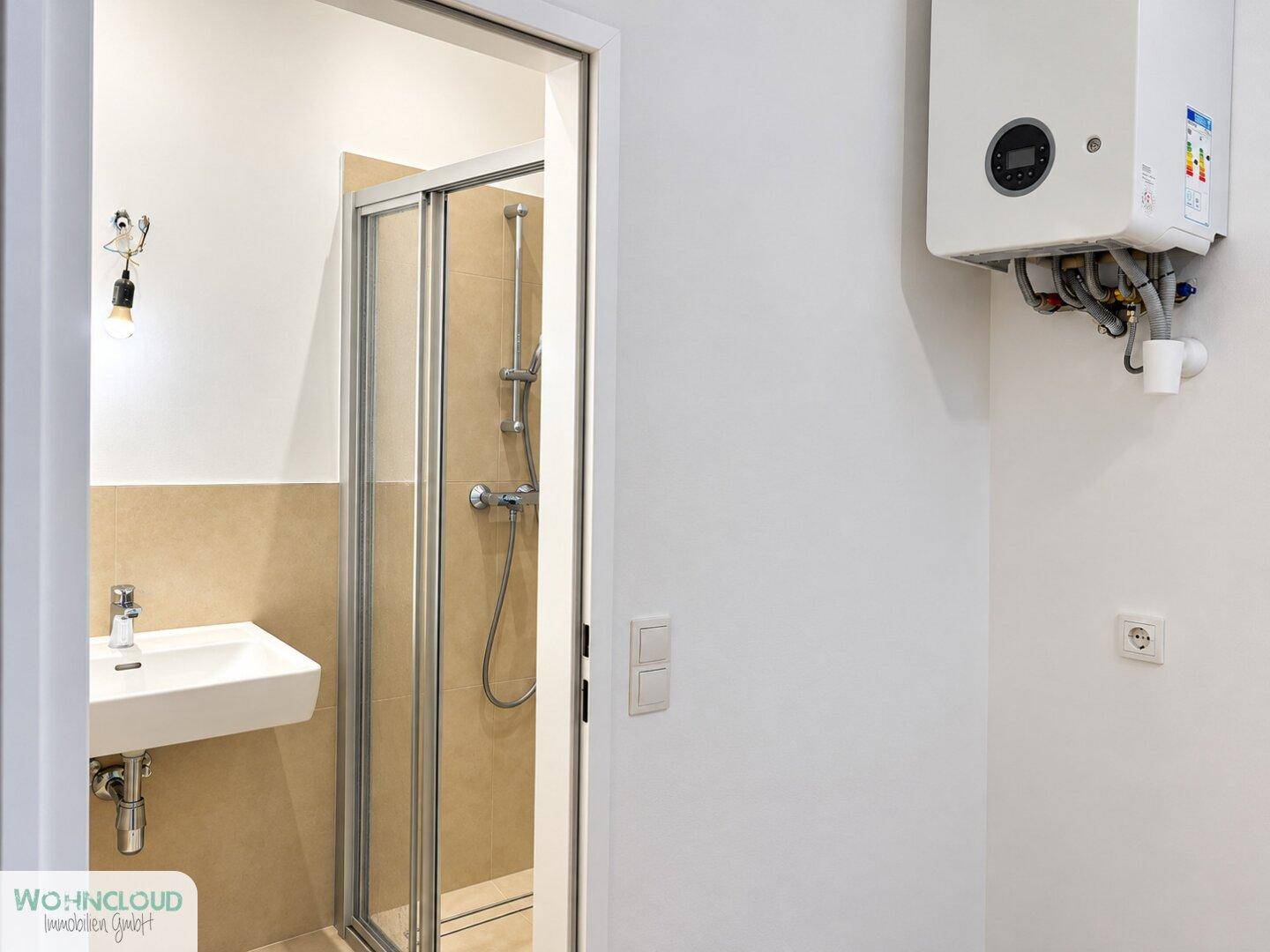 Eingangsbereich zum Badezimmer mit Warmwasserbereiter an der Wand und Duschkabine.