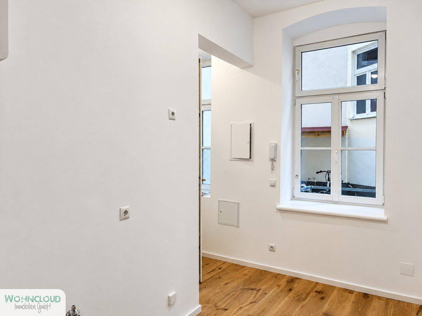 Heller Raum mit Holzboden, Fenster und verschiedenen Anschlüssen an den weißen Wänden.