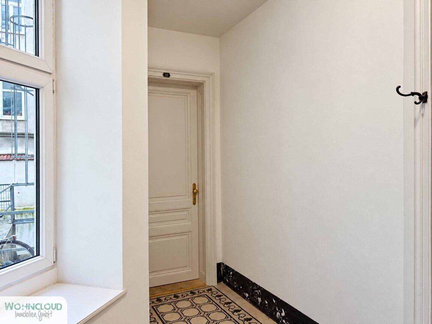 Heller Eingangsbereich mit dekorativem Fliesenboden und einem Fenster, das Tageslicht spendet.