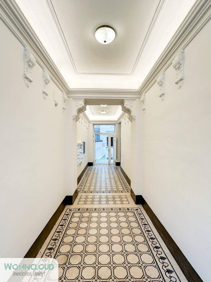 Eleganter Flur mit Stuckdecke und kunstvollem Fliesenboden, der zum Eingang führt.