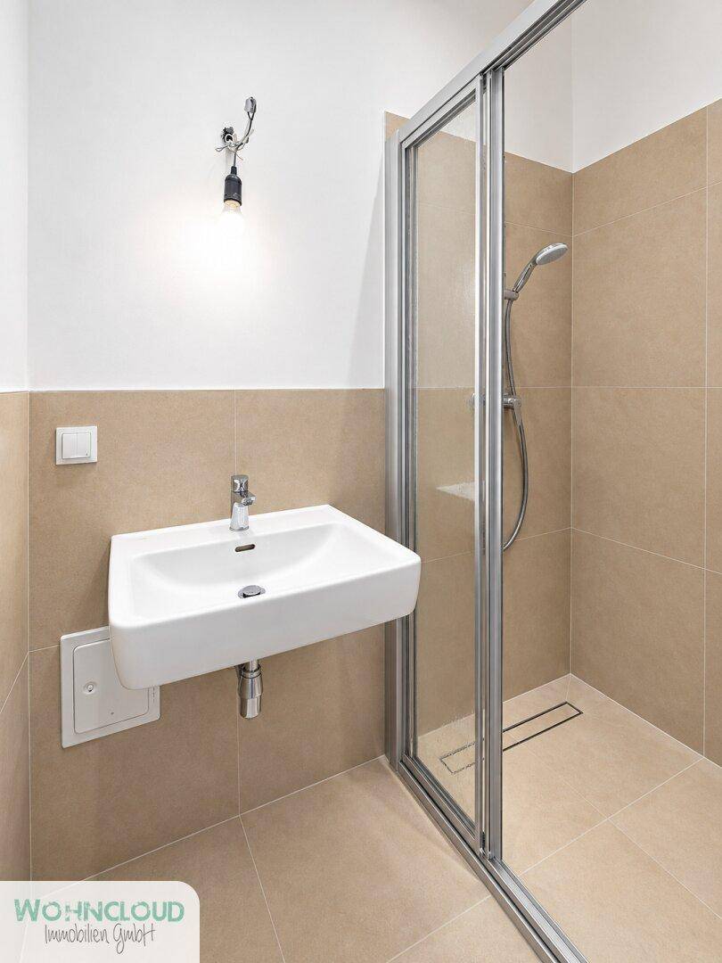 Modernes Badezimmer mit beigefarbenen Fliesen, einer Duschkabine und einem einzelnen Waschbecken.