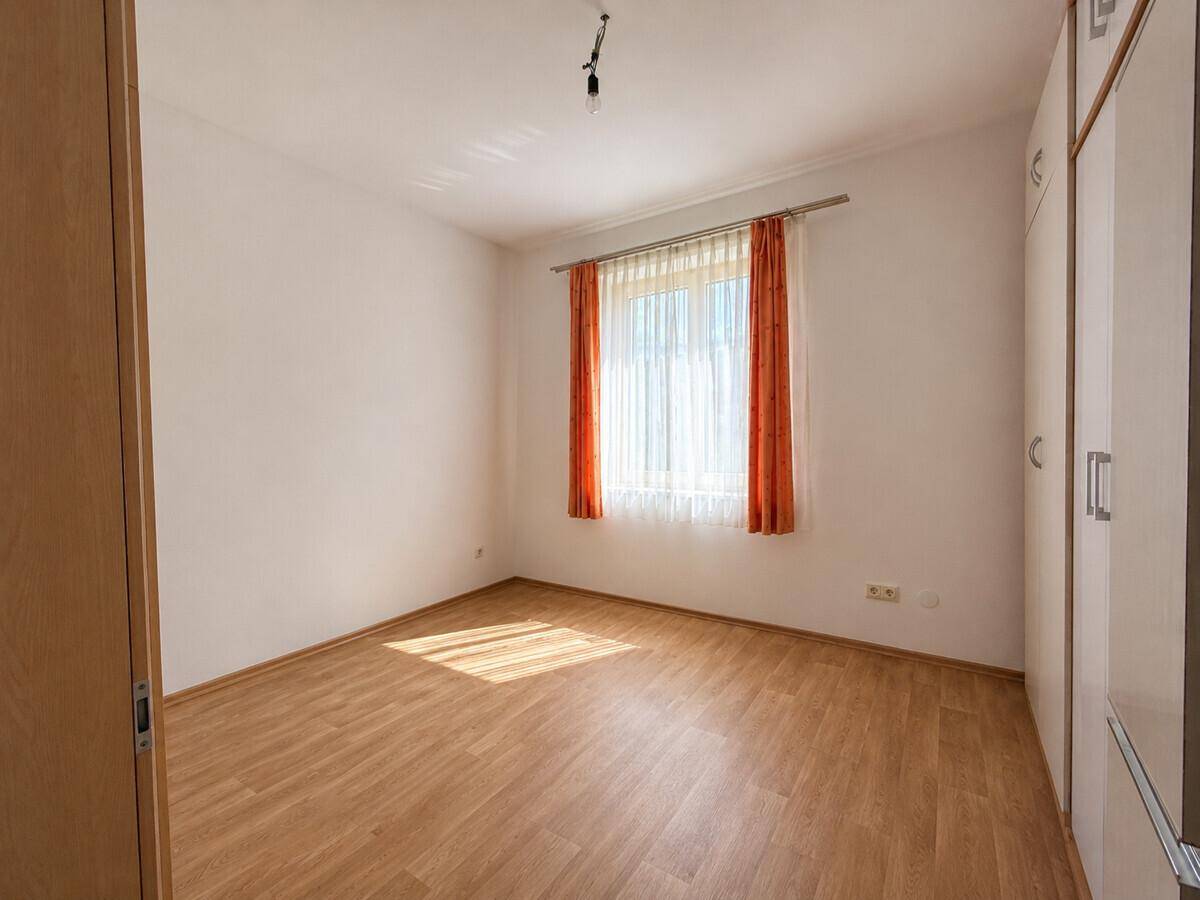 Helles Schlafzimmer mit Holzboden, großem Fenster und Einbauschrank.