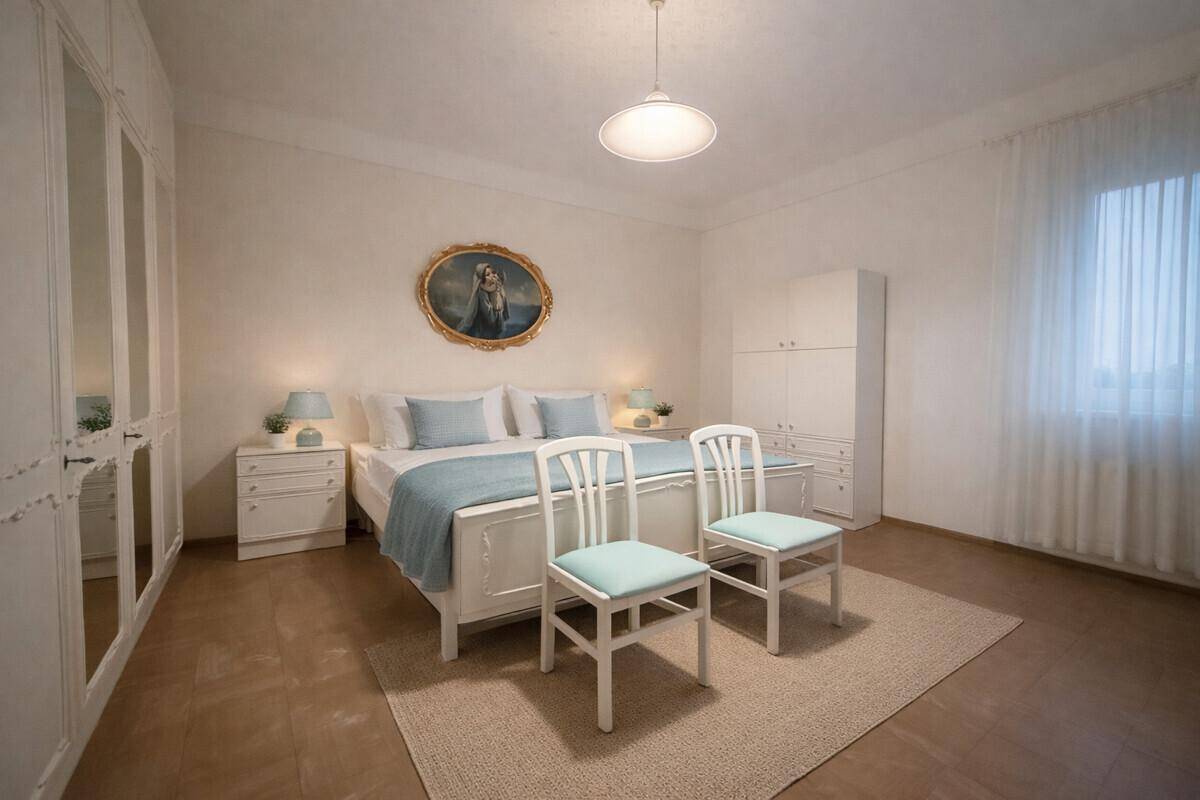 Helles Schlafzimmer mit weißem Doppelbett, Spiegelschränken und großem Fenster mit Vorhängen.