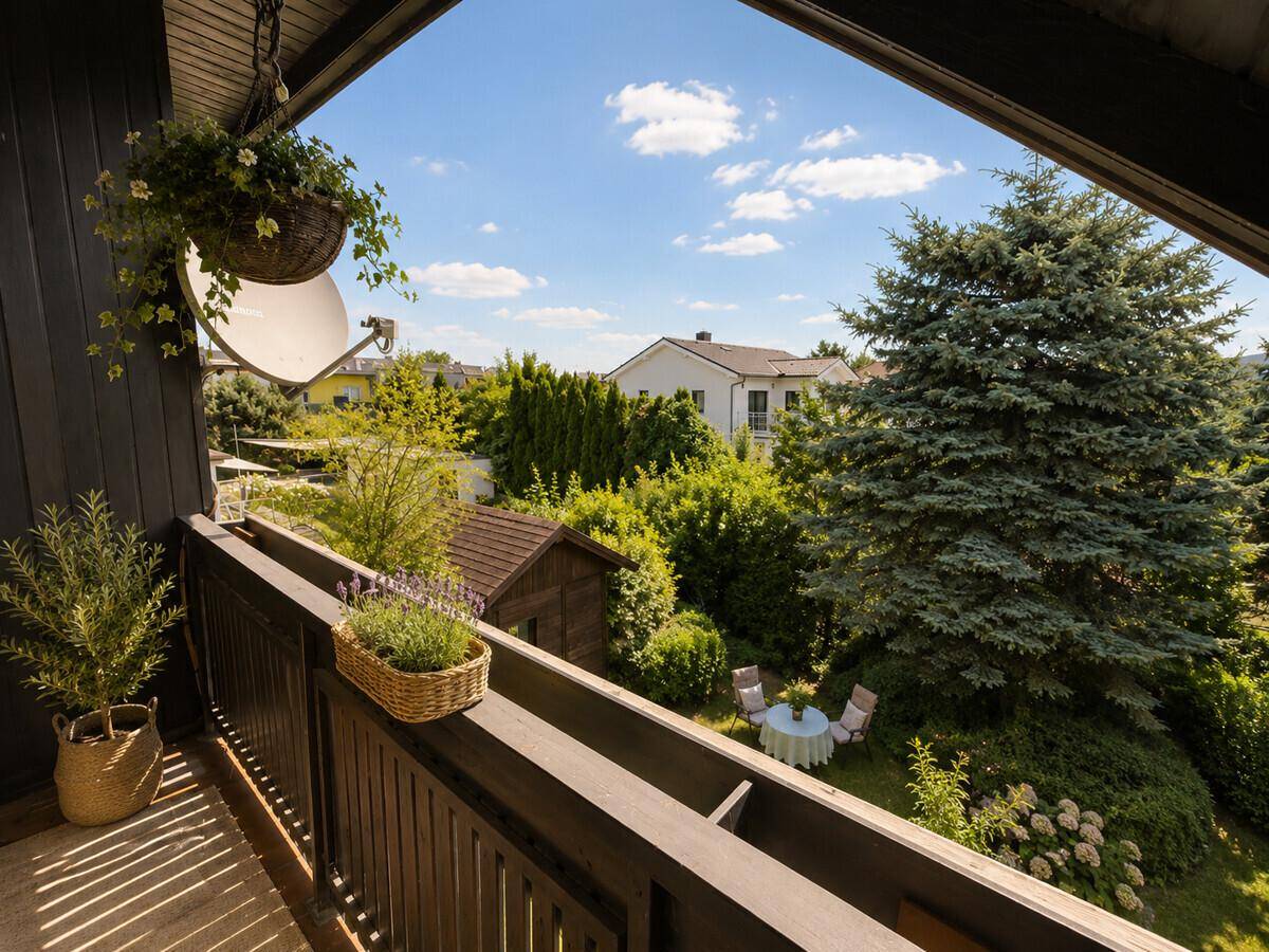 Geräumiger Balkon mit Holzboden, Blumen und weitem Blick über die Umgebung.