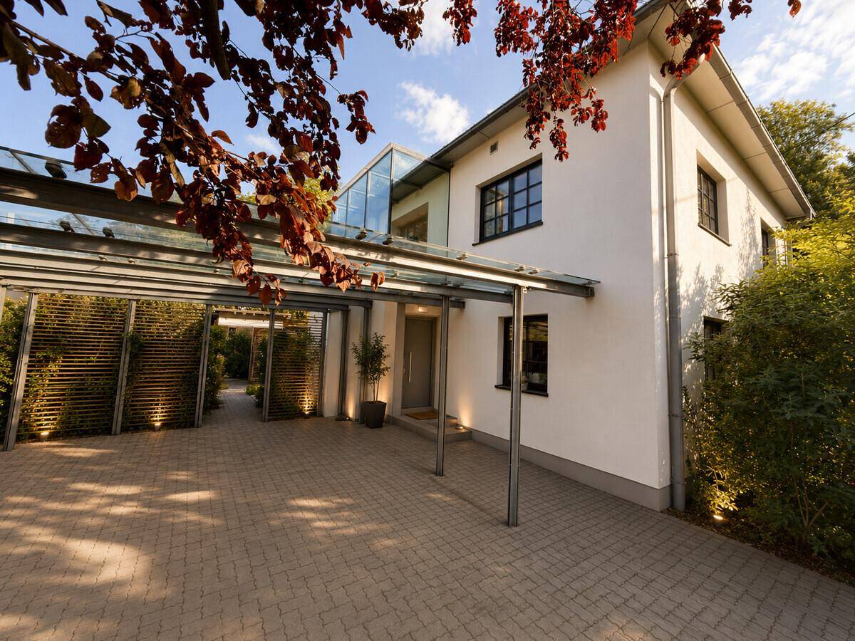 Modernes Wohnhaus mit Carport und Glasdach, umgeben von gepflegter Bepflanzung.