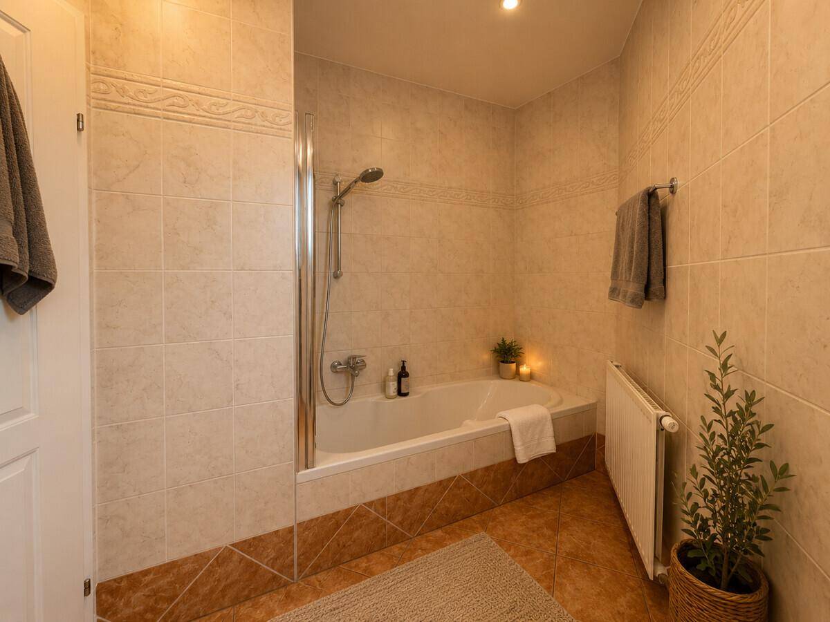 Badezimmer mit Badewanne und Duschbereich, gefliesten Wänden und Boden.