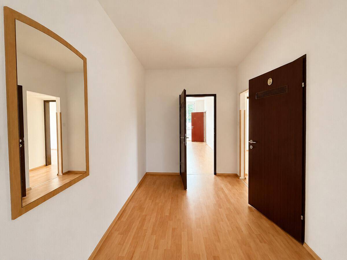 Langer Flur mit Laminatboden, weißen Wänden und einem großen Spiegel an der Seite.