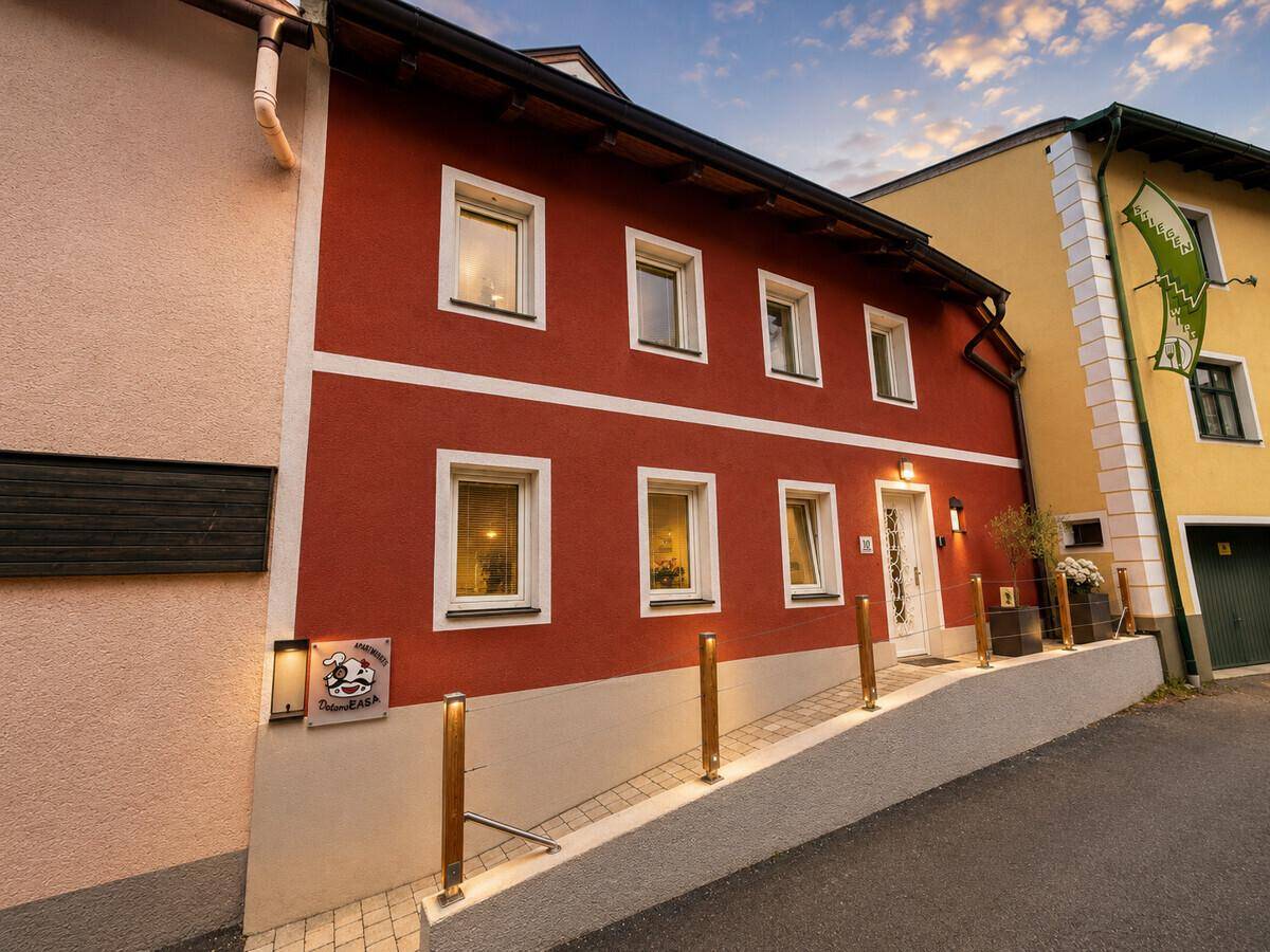 Rote Fassade eines Gebäudes bei Sonnenuntergang mit beleuchtetem Eingangsbereich und Rampe.