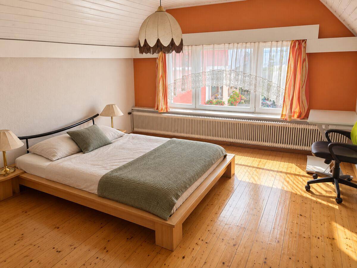 Helles Schlafzimmer mit Holzboden, Dachschräge und großem Fenster.