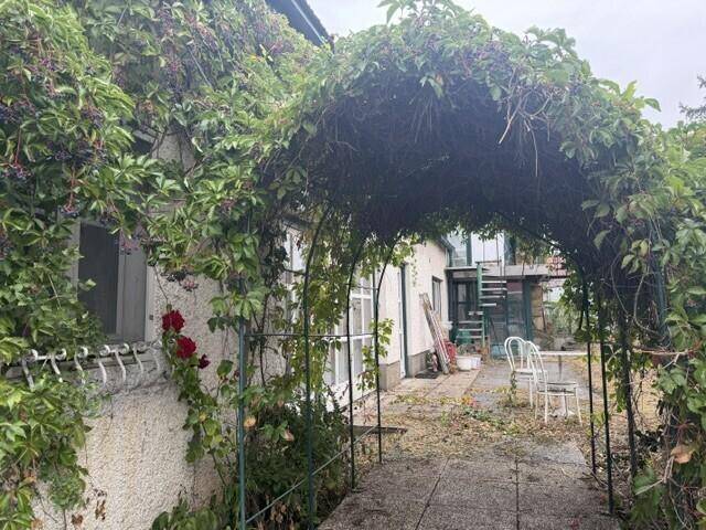 Begrünter Gartenweg mit Rankenbogen und kleiner Sitzecke im Freien.