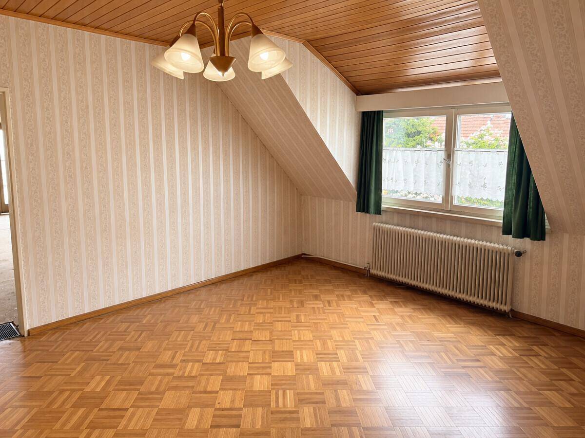 Geräumiges Zimmer mit Parkettboden, gestreifter Tapete und Dachschräge.
