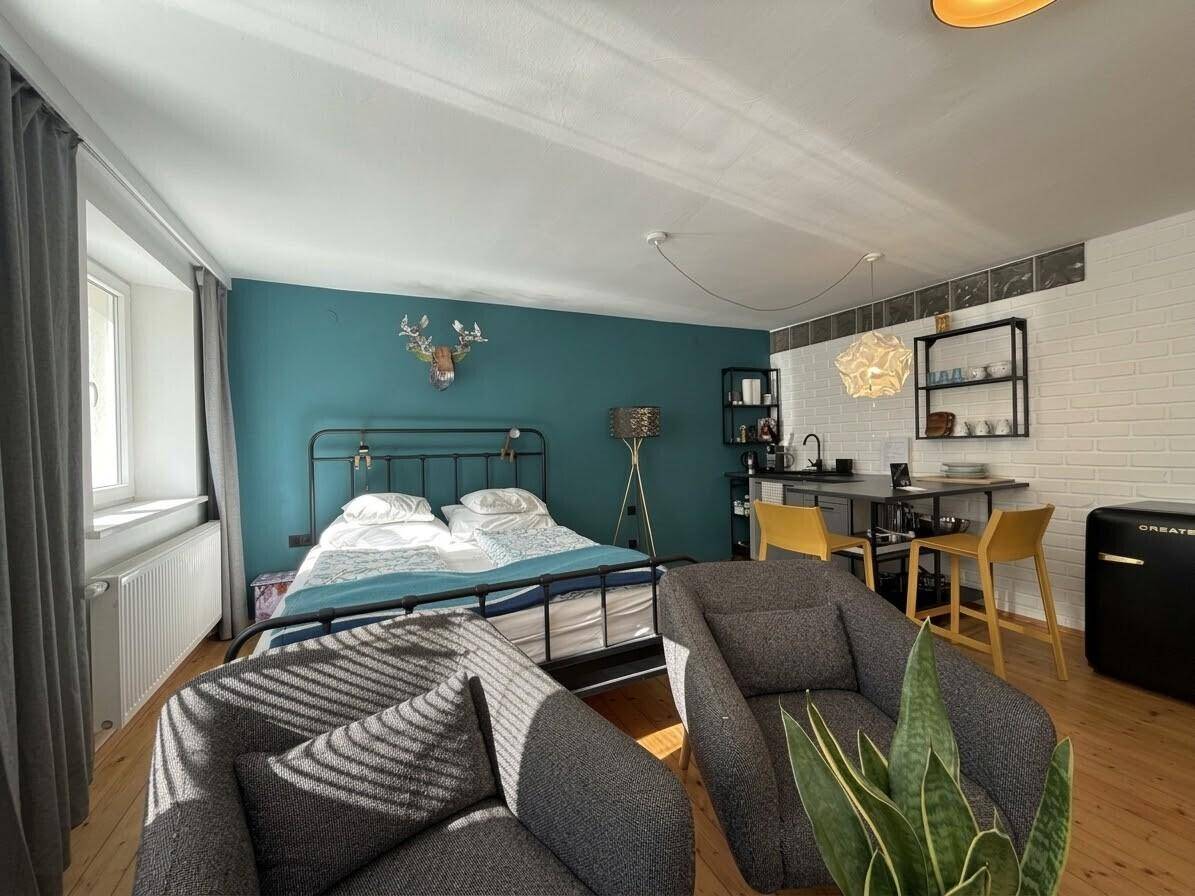 Gemütliches Studio-Apartment mit Holzboden, Schlafbereich und kleiner Küchenzeile.