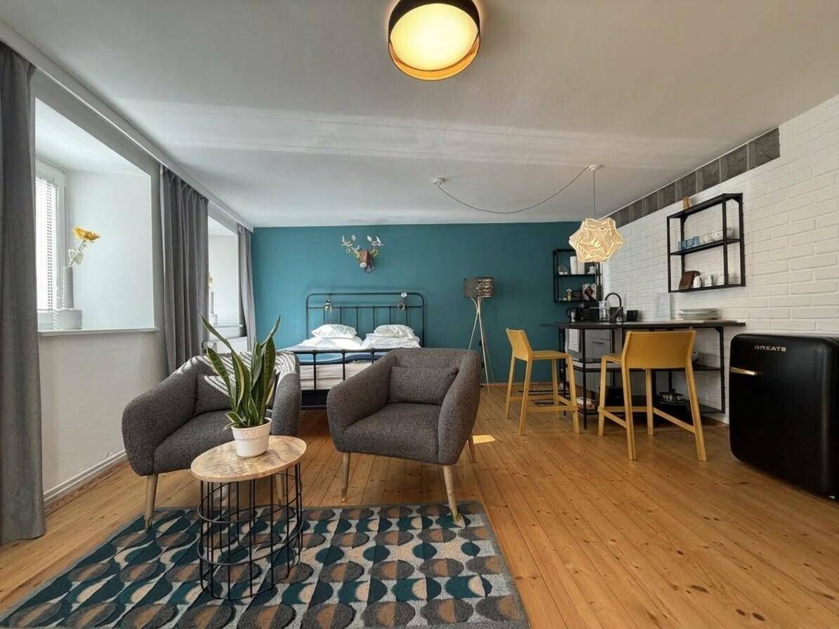 Helles Studio-Apartment mit Holzboden, Schlafbereich, Sitzecke und kleiner Küchenzeile.