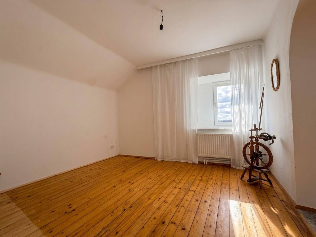 Heller Raum mit Holzboden, Dachschräge und großem Fenster mit Ausblick.