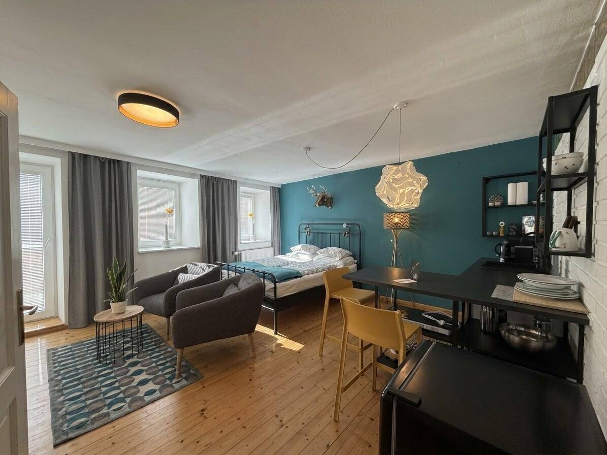 Geräumiges Studio-Apartment mit Holzboden, Schlafbereich, Sitzecke und integrierter Küchenzeile.