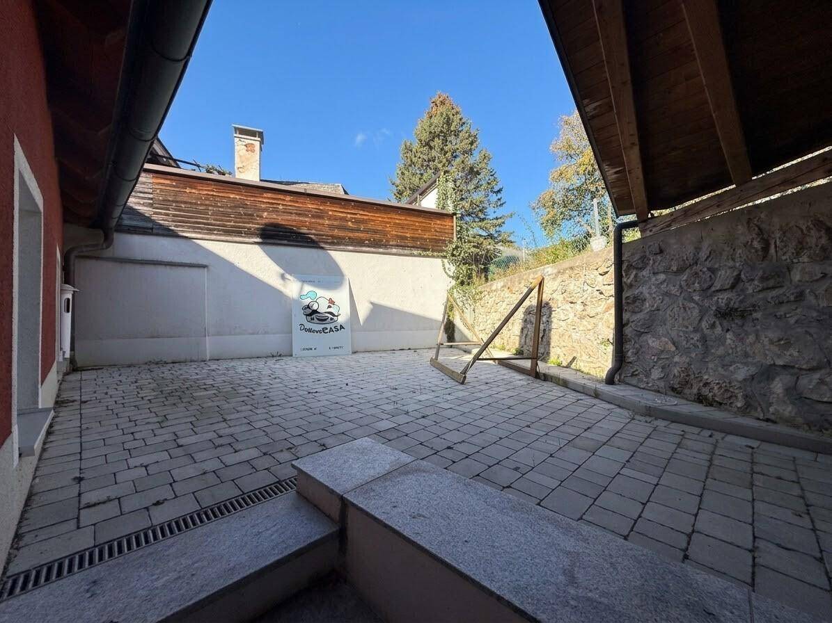 Gepflasterter Innenhof mit Steinmauern und einem Holzzaun unter blauem Himmel.