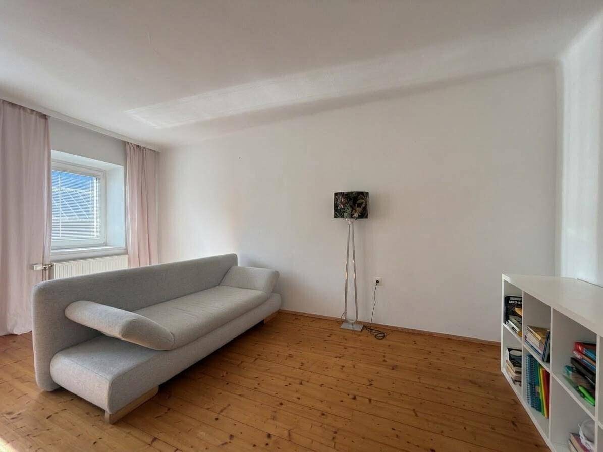 Heller Raum mit Holzboden, großem Fenster und einfacher Einrichtung.