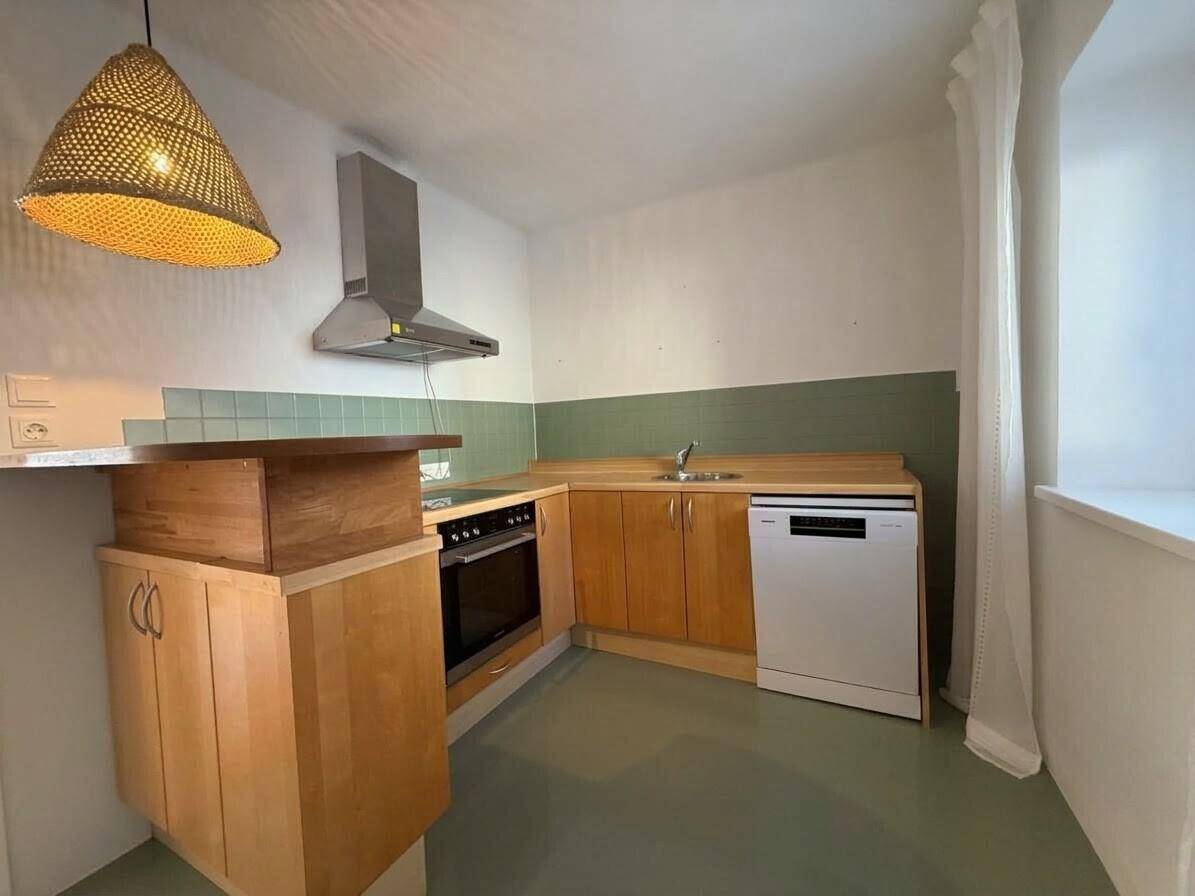 Funktionale Küche mit Holzschränken, Spülmaschine und Dunstabzugshaube.