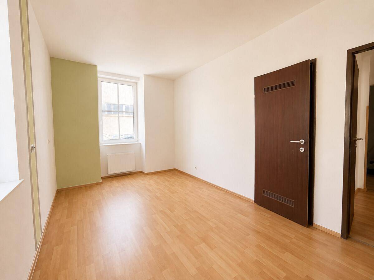 Leeres Zimmer mit Laminatboden, weiß gestrichenen Wänden und einer grünen Akzentwand.