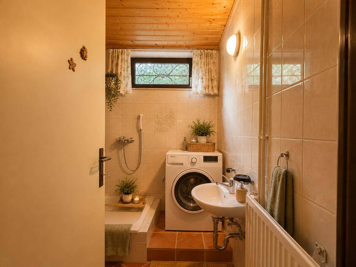 Kleines Badezimmer mit Badewanne, Waschmaschine und Fenster.